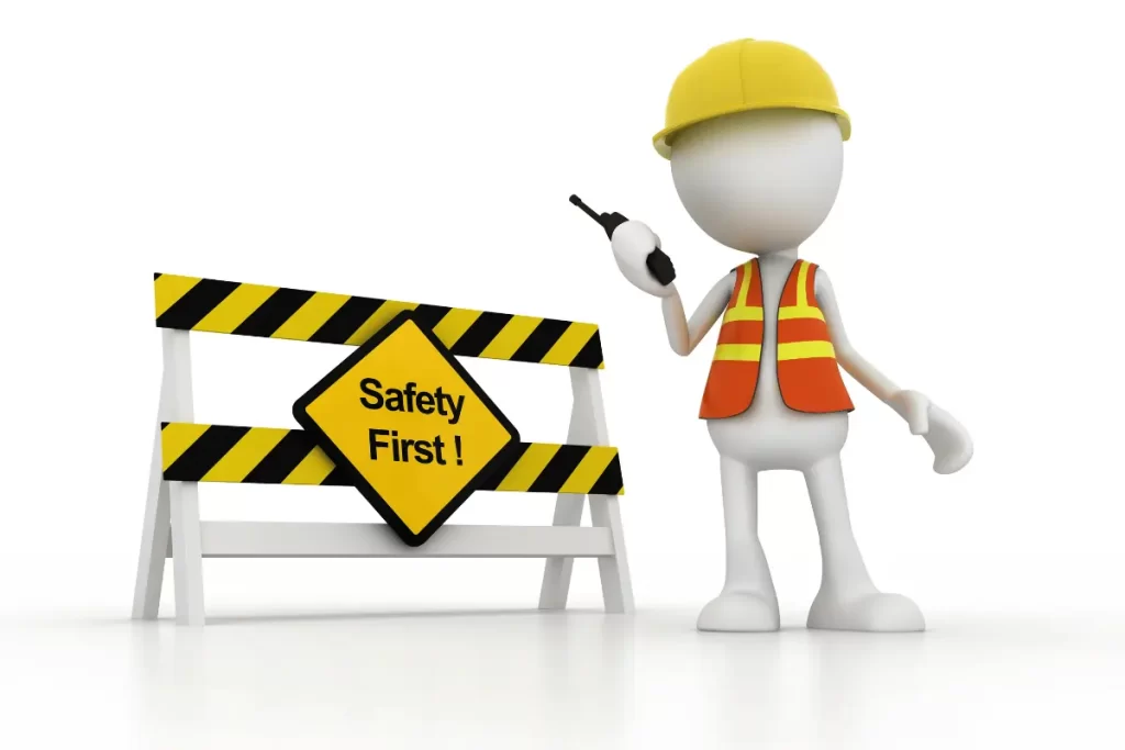 omino con casco e gilet di sicurezza vicino ad una transenna con la scritta "safety first"