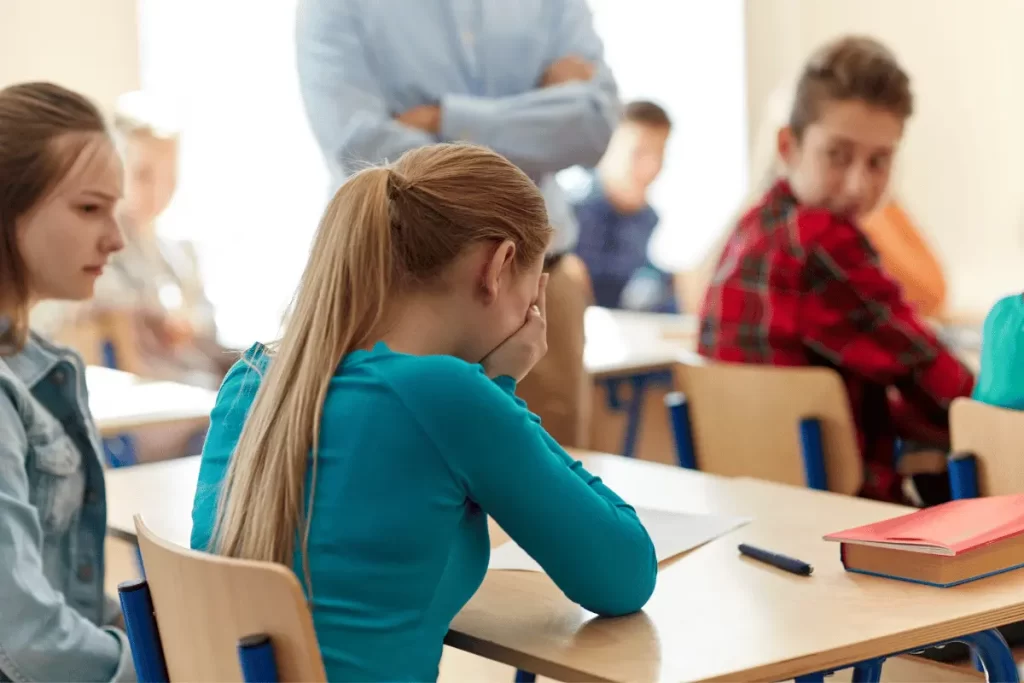 alunna seduta al banco in classe si copre il volto