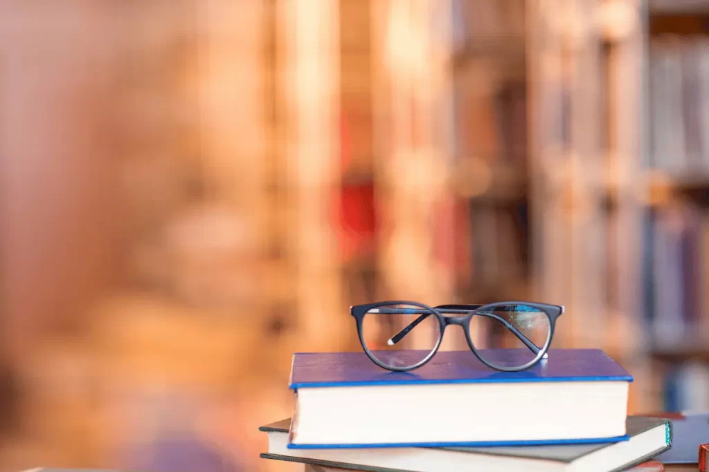 occhiali sopra un libro, con sullo sfondo scaffali di libri sfocati
