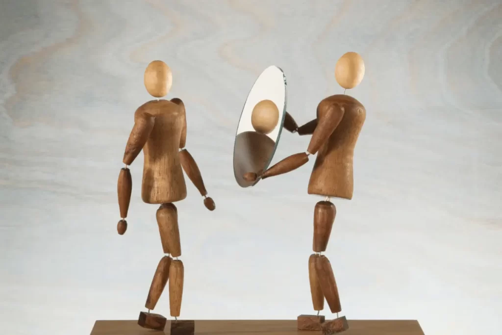 un omino di legno con uno specchio in mano rivolto verso un altro omino