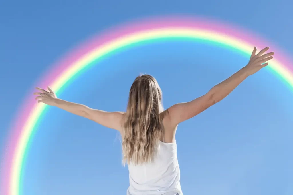una ragazza con le braccia aperte guarda un arcobaleno
