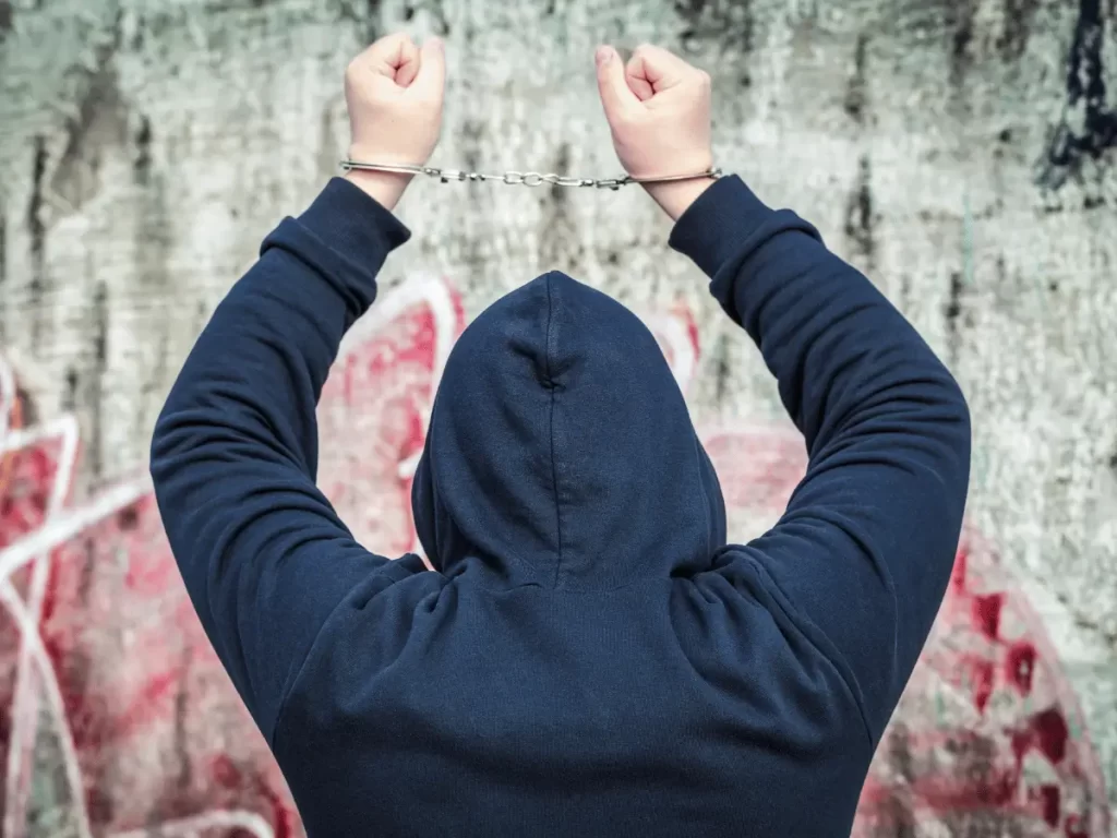 un ragazzo di spalle con le mani ammanettate alzate