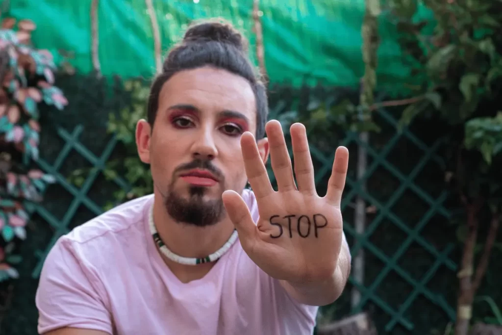 un uomo truccato mostra la mano con su scritto "stop"