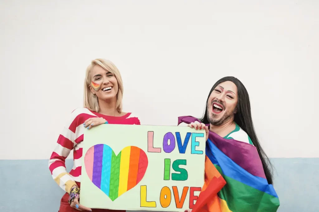 una donna e un uomo reggono un cartellone con un cuore arcobaleno e la scritta "Love is love"