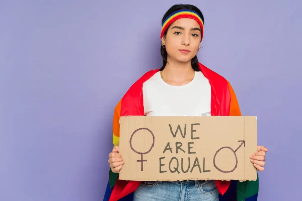 una ragazza con bandiera e capellino arcobaleno regge un cartone con su scritto "we are equal"